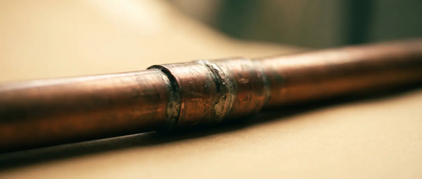 Close-up illustration of a soldered copper pipe joint, abstract horizontal band of light and shadow, not a photograph of an actual repair